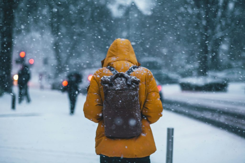 Persona caminando con una campera amarilla en la nieve, simulando ventas en frio.